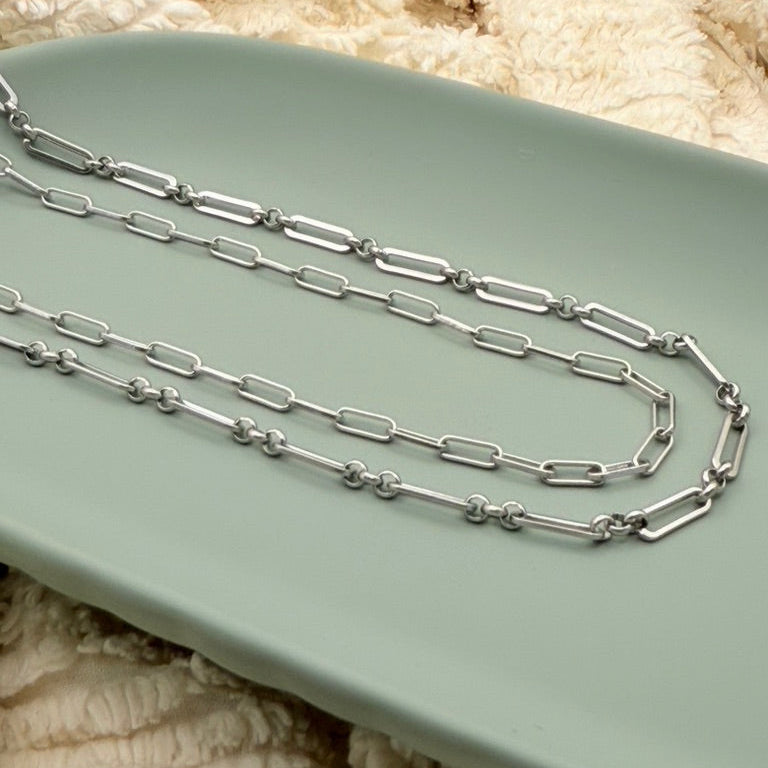 Close-up of a person wearing two silver necklaces with a blurred background