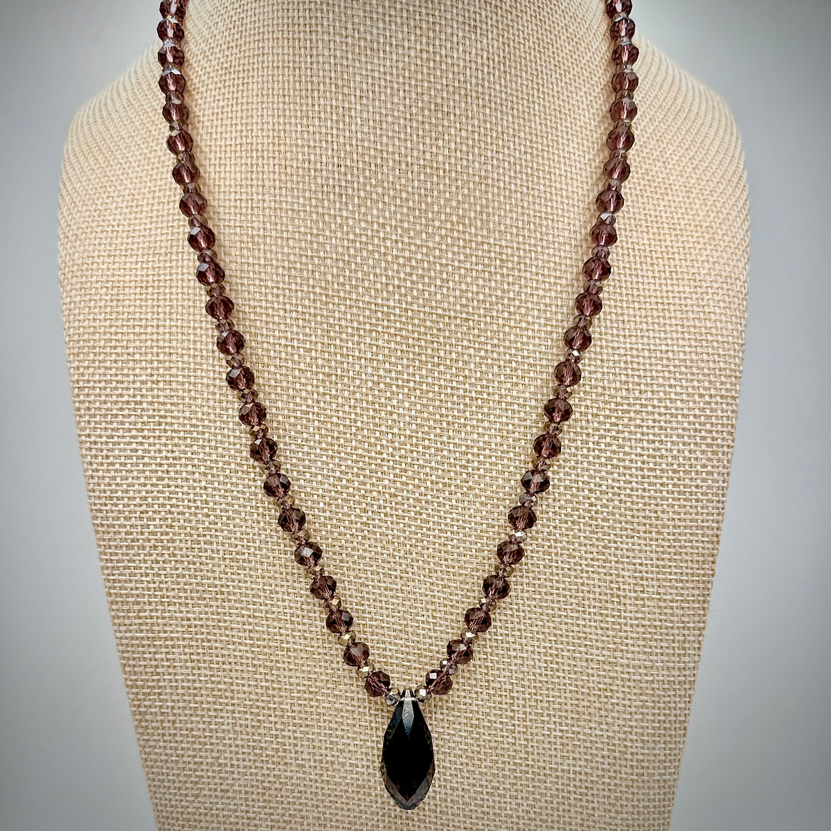 Necklace with brown beads and a black pendant on a beige mannequin bust.