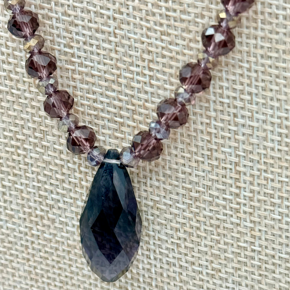 Necklace with dark purple beads and a large faceted stone on a textured beige background
