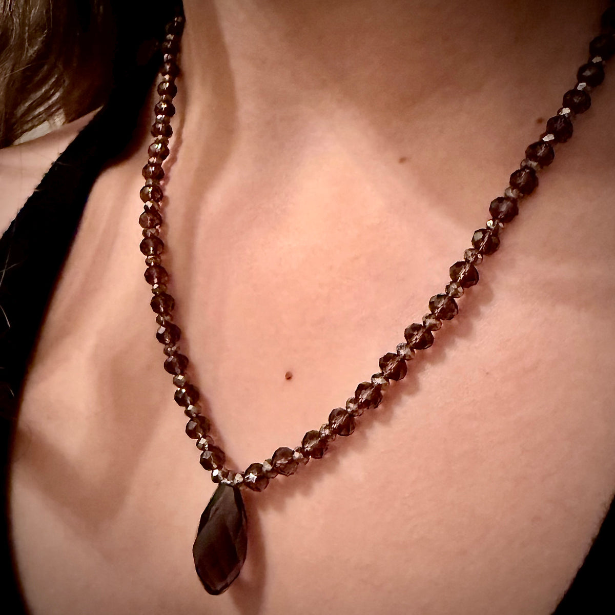 Close-up of a necklace with dark beads and a teardrop pendant on a person's neck.