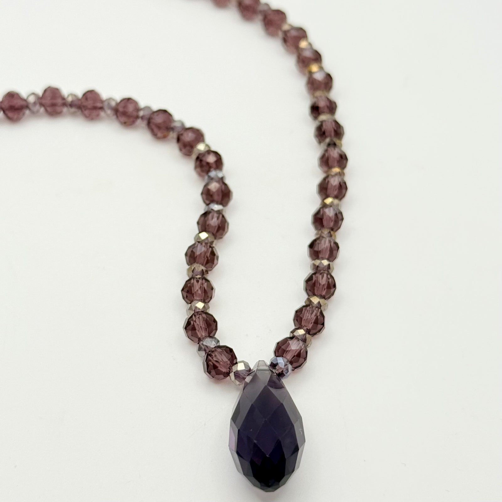 Close-up of a necklace with dark beads and a teardrop pendant on a person's neck.