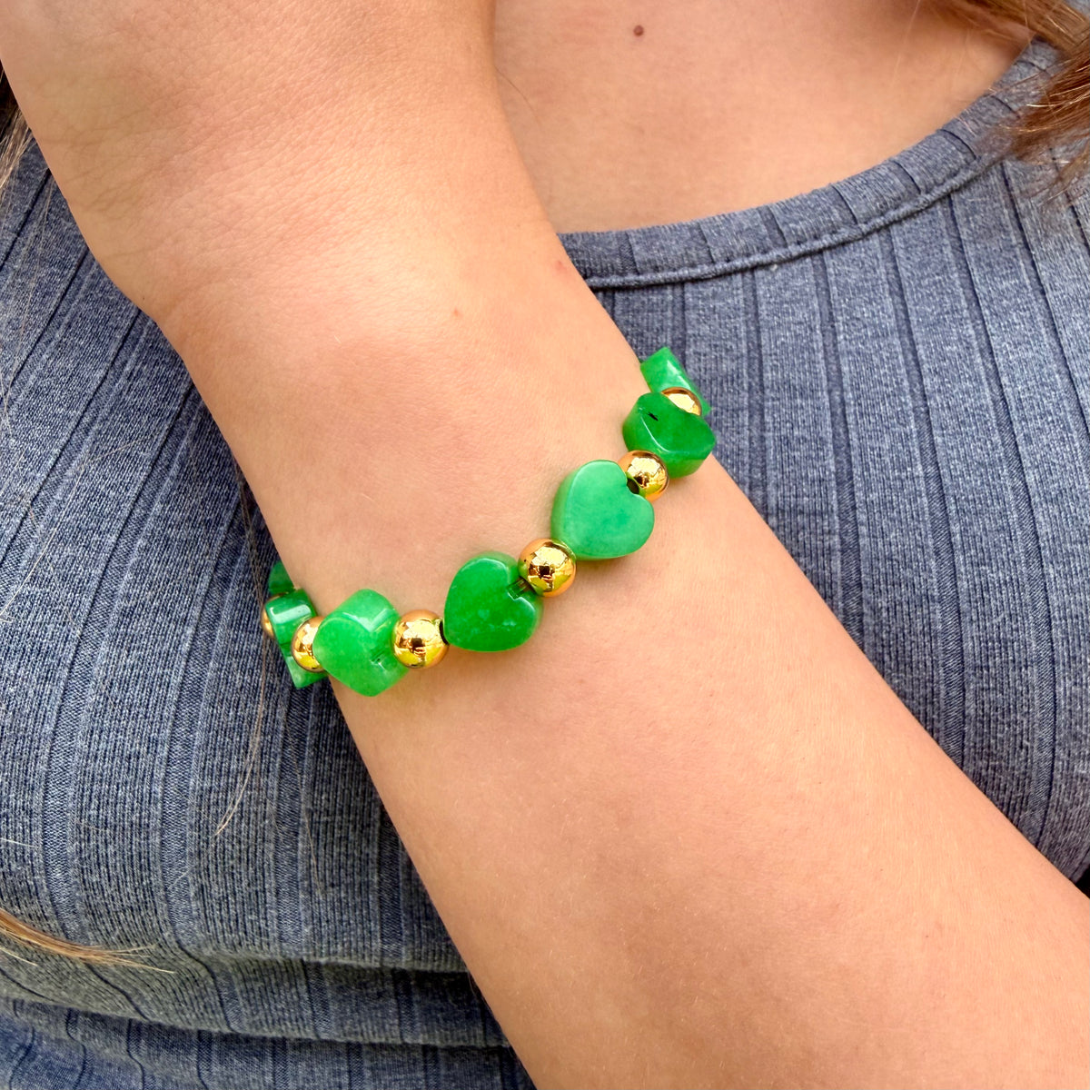 Green beaded bracelet with gold accents on a wrist against a denim background