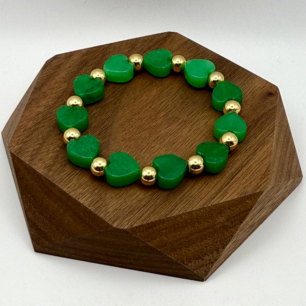 Green heart-shaped beaded bracelet with gold accents on a wooden stand.