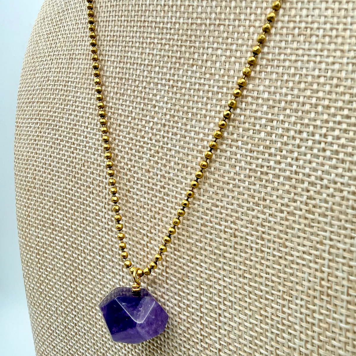 Necklace with a purple pendant on a beige mannequin bust against a light blue background
