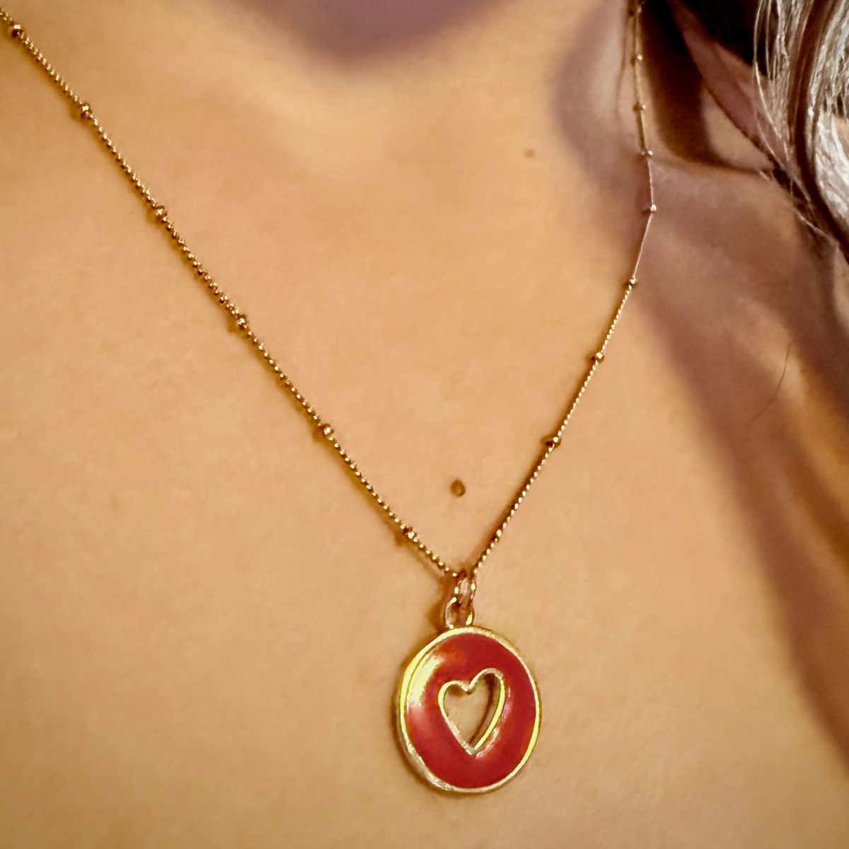 Dainty 18k gold-plated satellite chain necklace featuring a circular red enamel charm with a gold heart in the center.