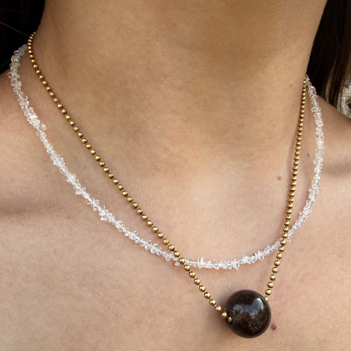 Necklace with gold beads and a dark stone on a person's neck