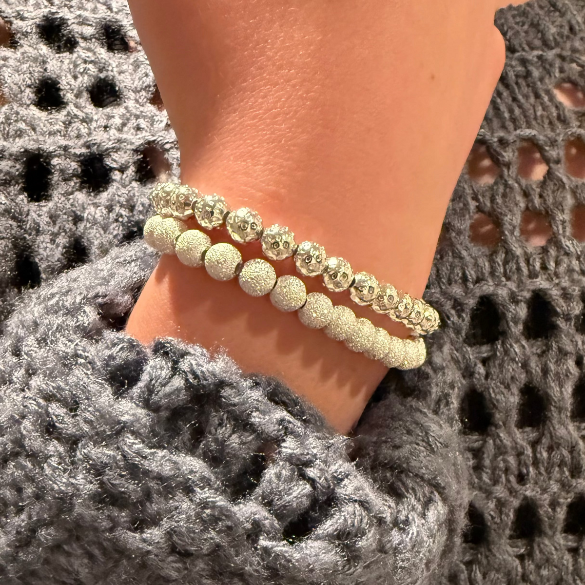 Close-up of a person wearing a silver bracelet on a textured gray sweater.