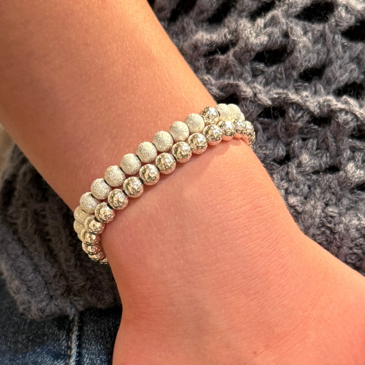 Close-up of a person's wrist wearing a beaded bracelet with a textured gray fabric background.