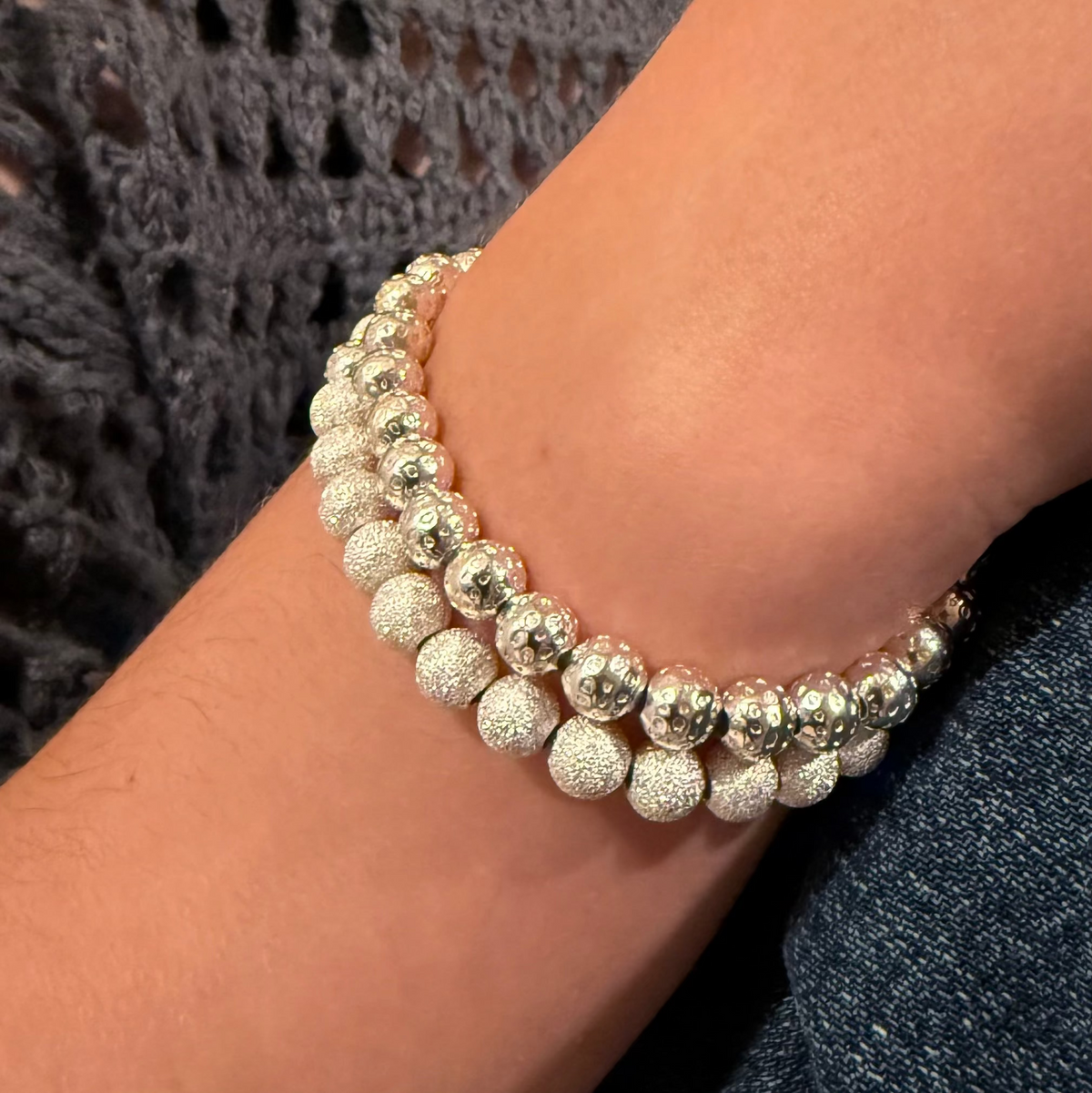 Close-up of a wrist wearing two beaded bracelets with a textured background