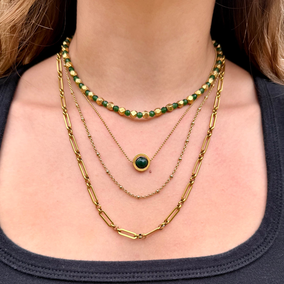 Close-up of a person wearing multiple gold necklaces with green beads.