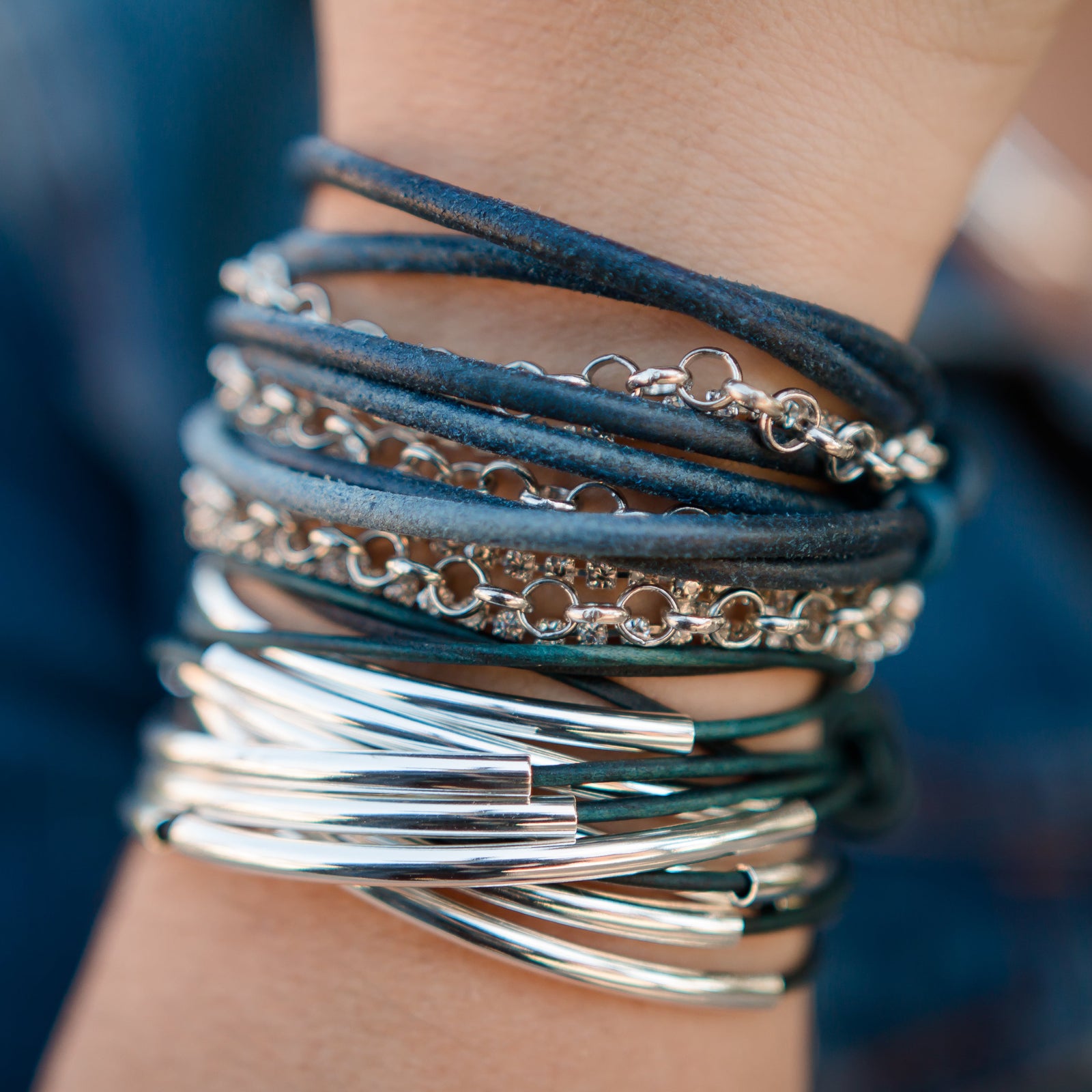 Stack of silver and leather bracelets on a wrist with a blurred background