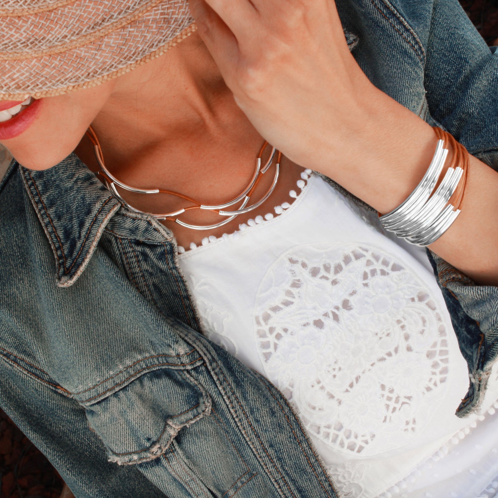 Person wearing a denim jacket, white lace top, and multiple bracelets on a blurred background
