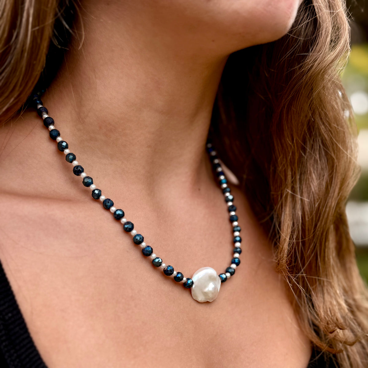 Close-up of a woman wearing a black beaded necklace with a large white pearl pendant.