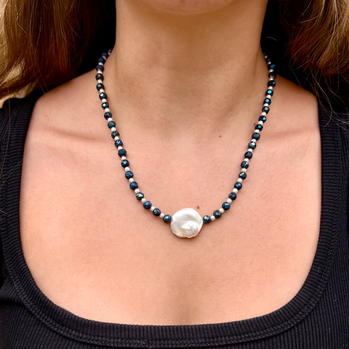 Necklace with a large white pearl pendant on a person wearing a black top.