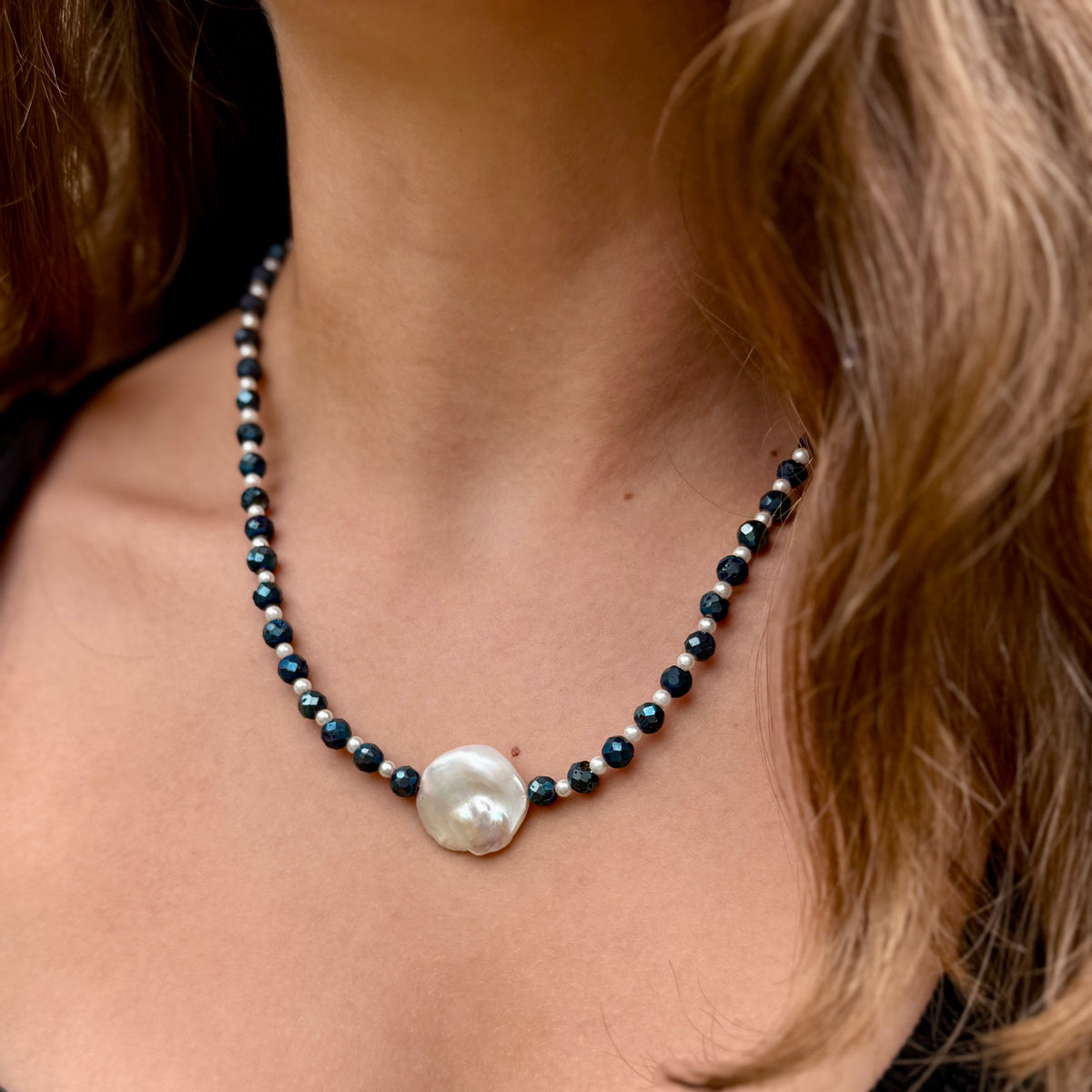 Close-up of a necklace with black beads and a large pearl on a person's neck.