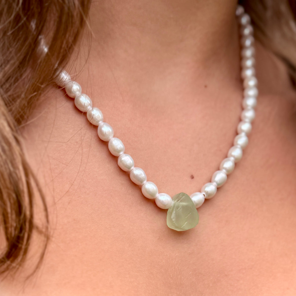 Pearl necklace with a green stone pendant on a person's neck