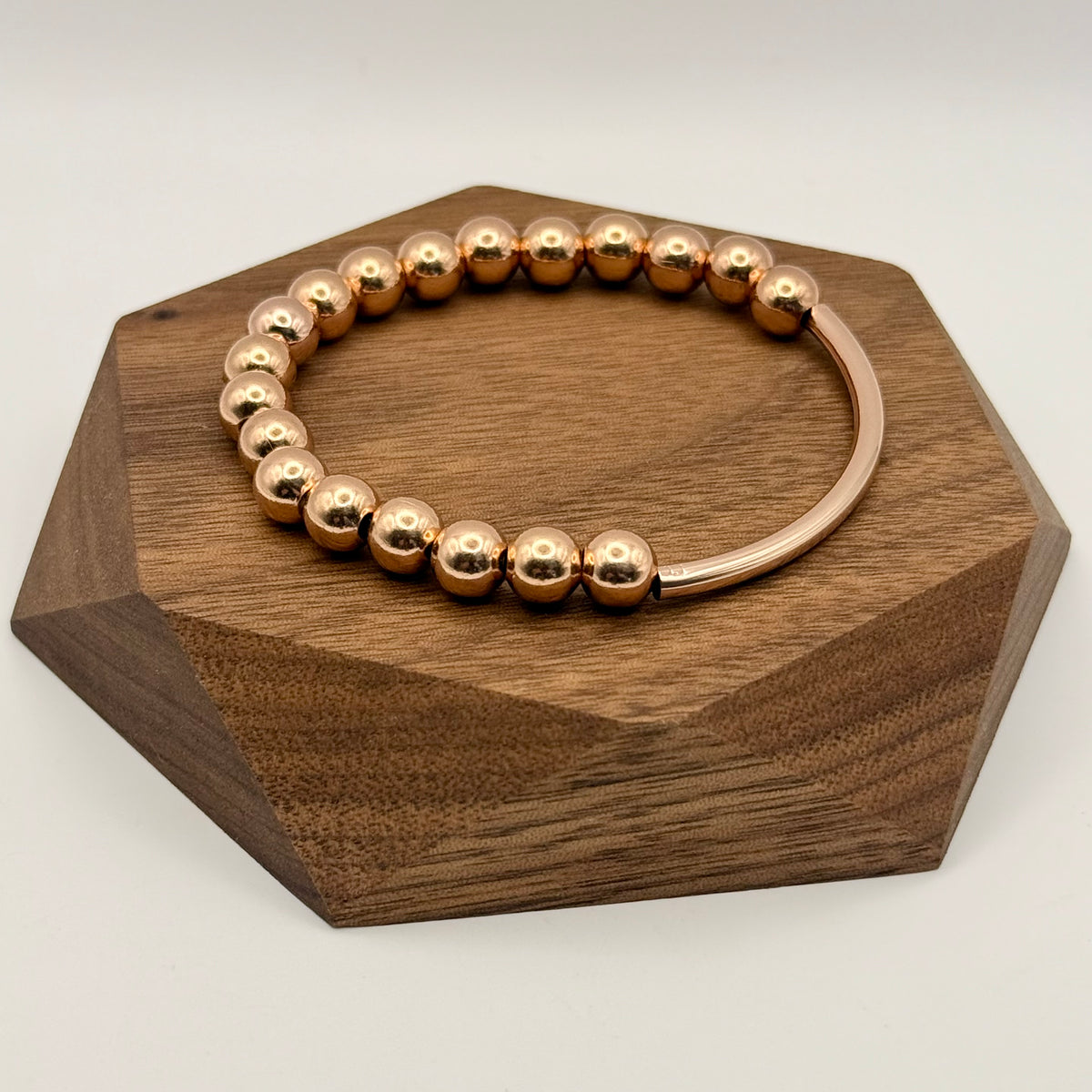 Rose gold beaded bracelet on a wooden hexagonal stand with a white background