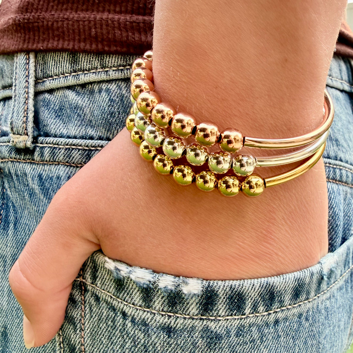 Gold beaded bracelets on a wrist with denim jeans in the background