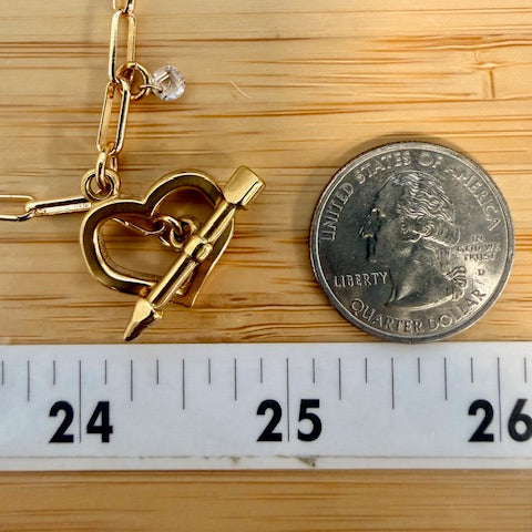 Gold bracelet with heart and arrow charm next to a quarter for scale on a wooden surface