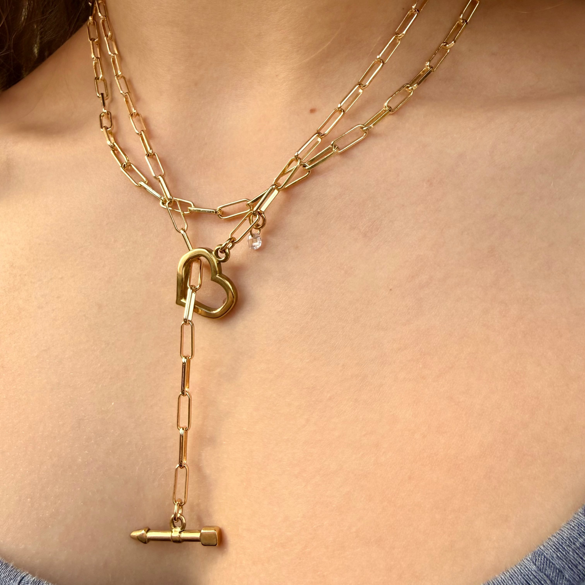 Gold chain necklace with heart and key pendant on a person wearing a blue top.