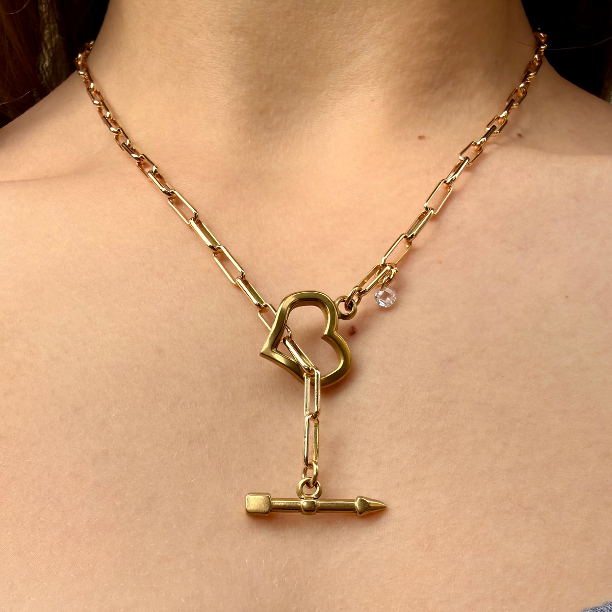 Gold necklace with a heart-shaped clasp worn by a person