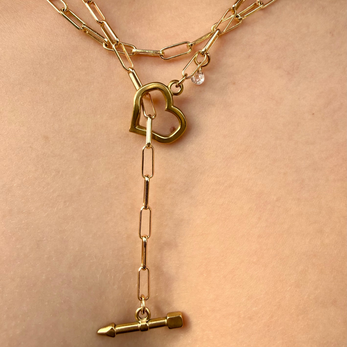 Gold chain necklace with heart and bullet pendant on a person's neck