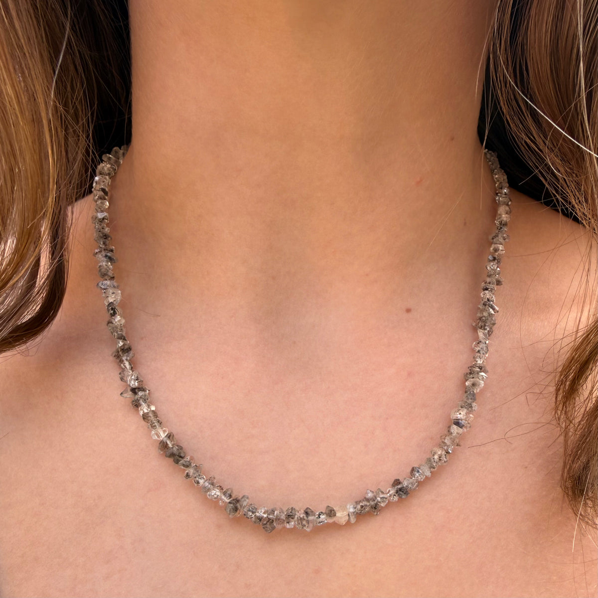 Necklace with small, faceted stones worn by a person with brown hair.