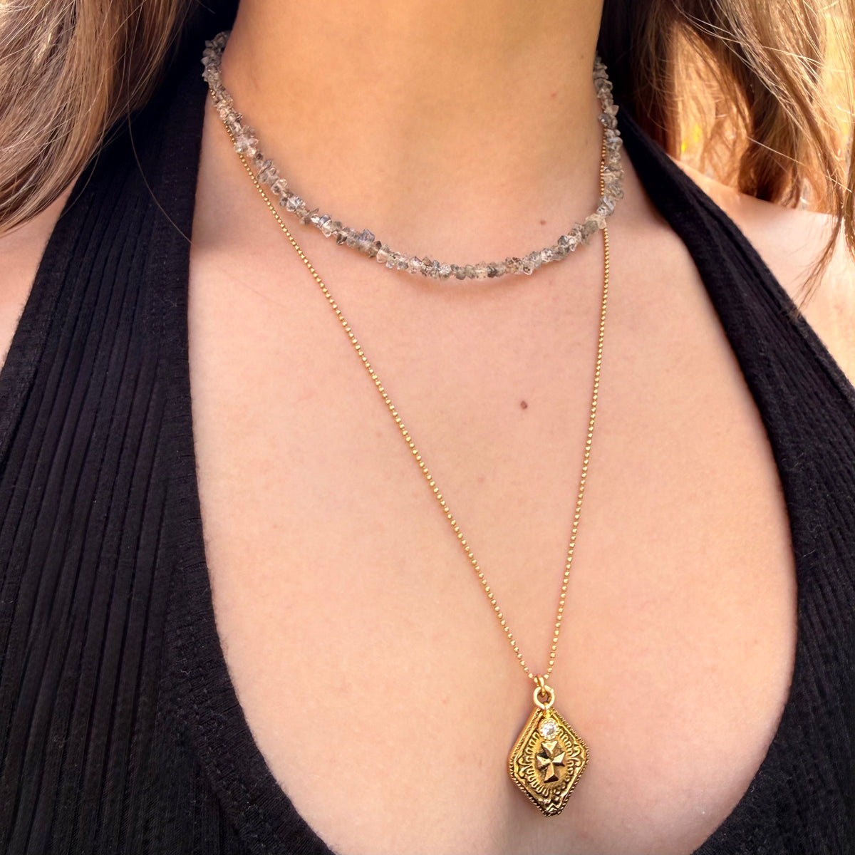 Gold necklace with a pendant worn by a person against a black background