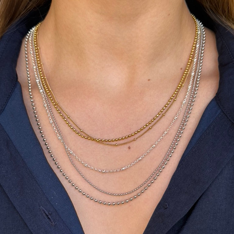 Close-up of a person wearing multiple necklaces with a blue shirt.