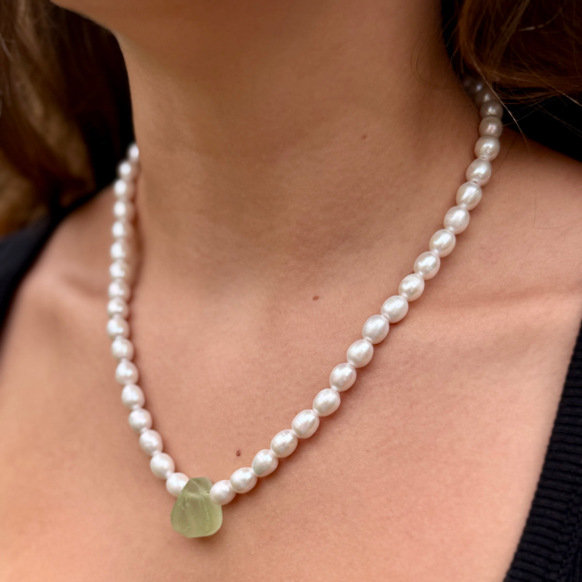 Pearl necklace with a green pendant worn by a person