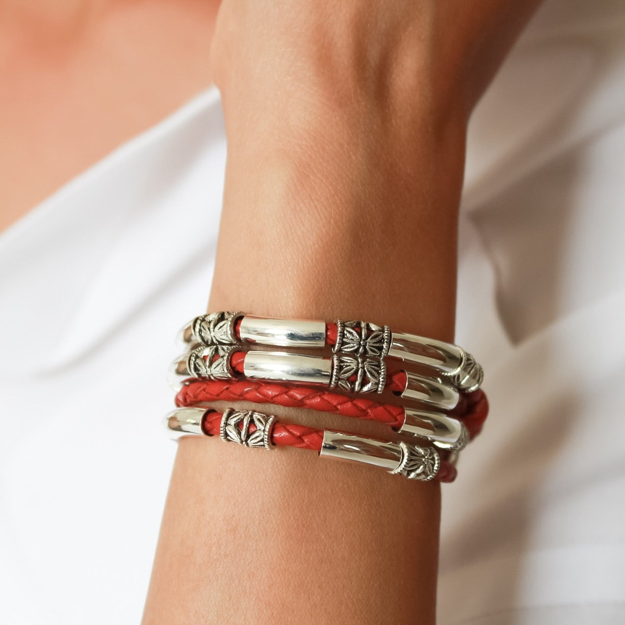 Silver and red bracelets on a wrist against a neutral background