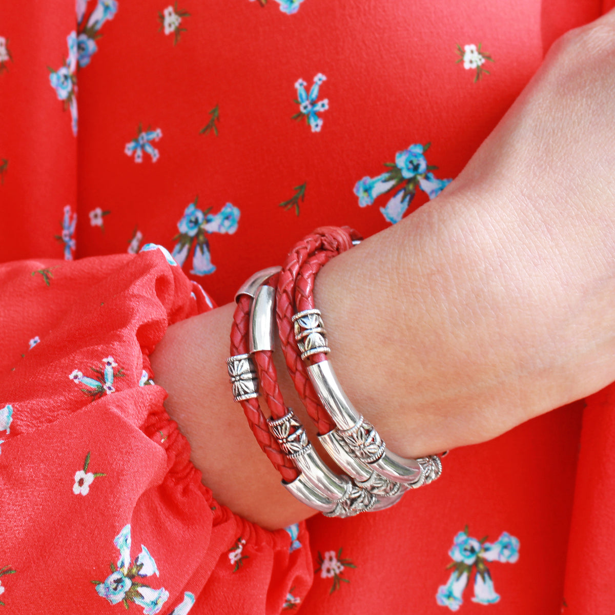 Red bracelet with silver accents on a wrist against a red floral background