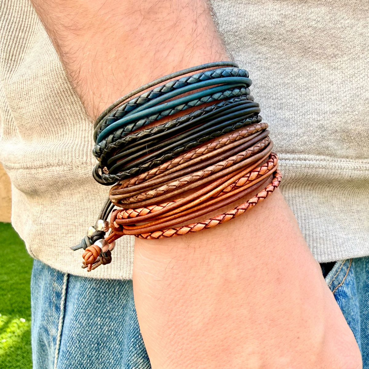 Close-up of a wrist wearing multiple braided leather bracelets with a blurred background.
