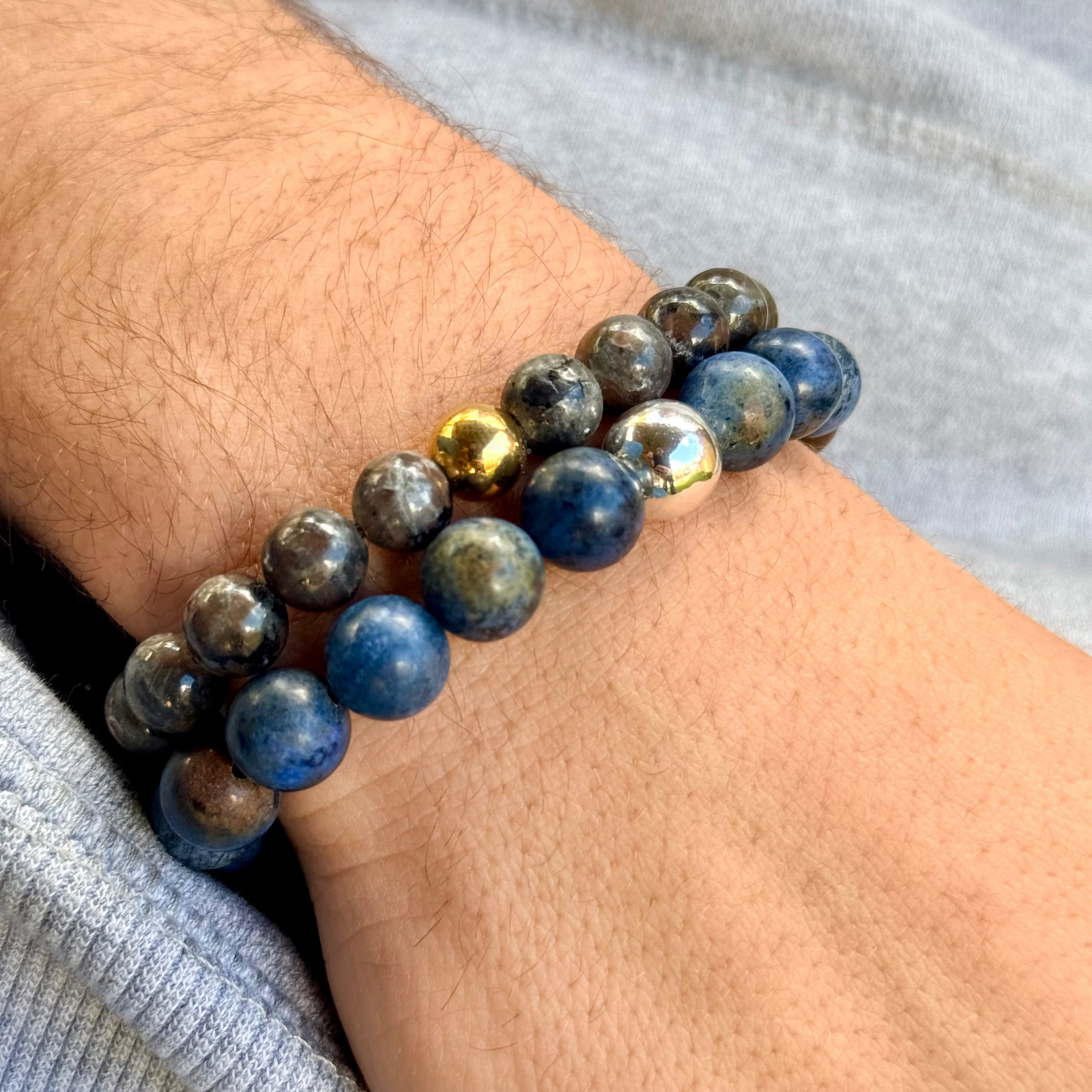 Close-up of a wrist wearing a stack of blue beaded bracelets with gold accents.