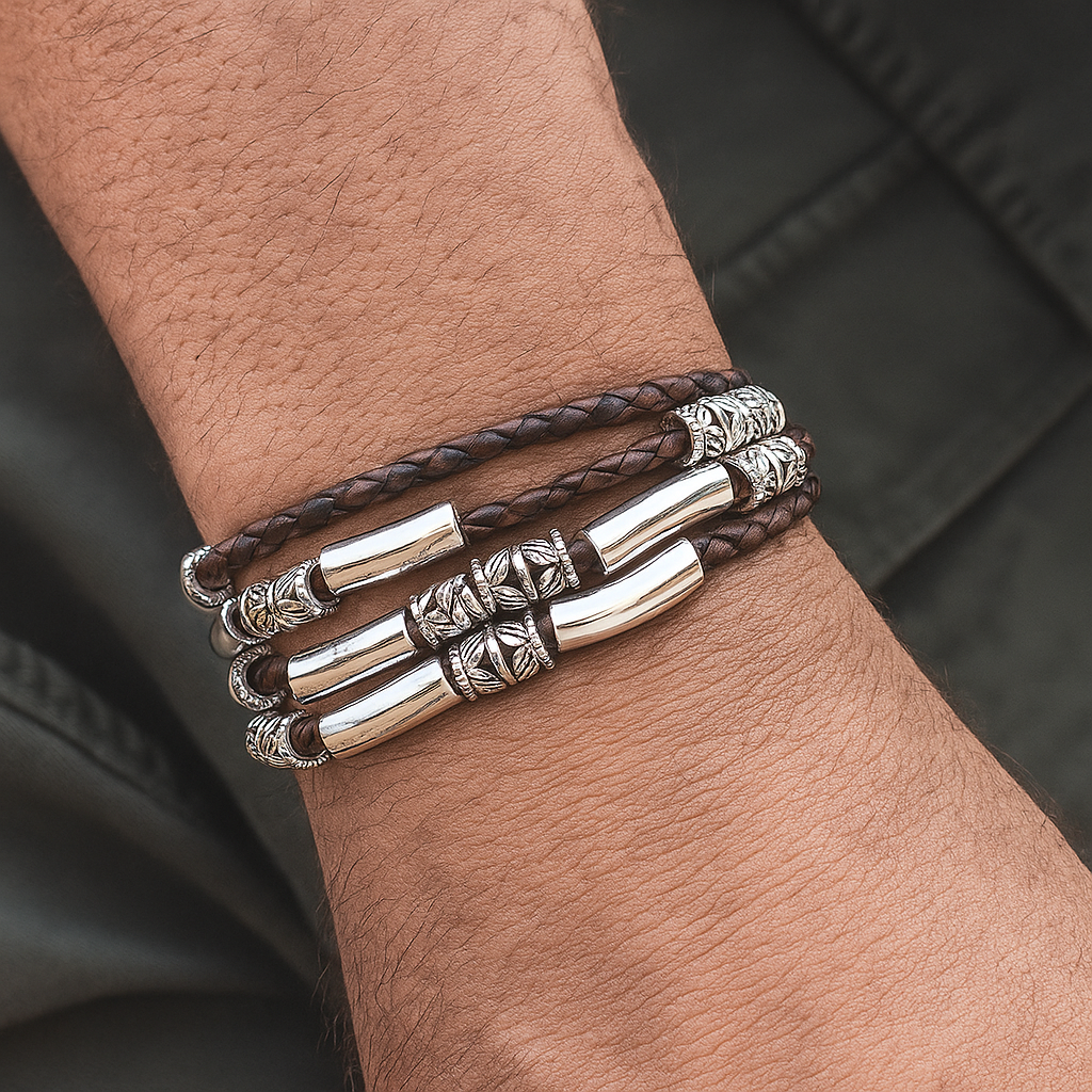 Three silver bracelets with leather strap on a wrist against a dark background