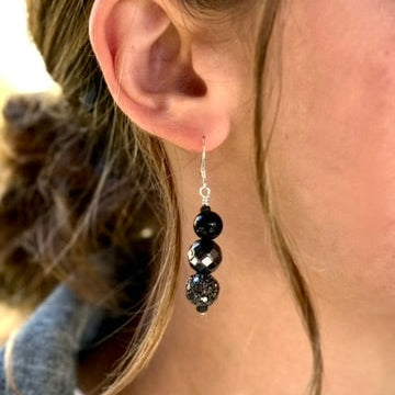 Close-up of an ear wearing a black beaded earring with a blurred background
