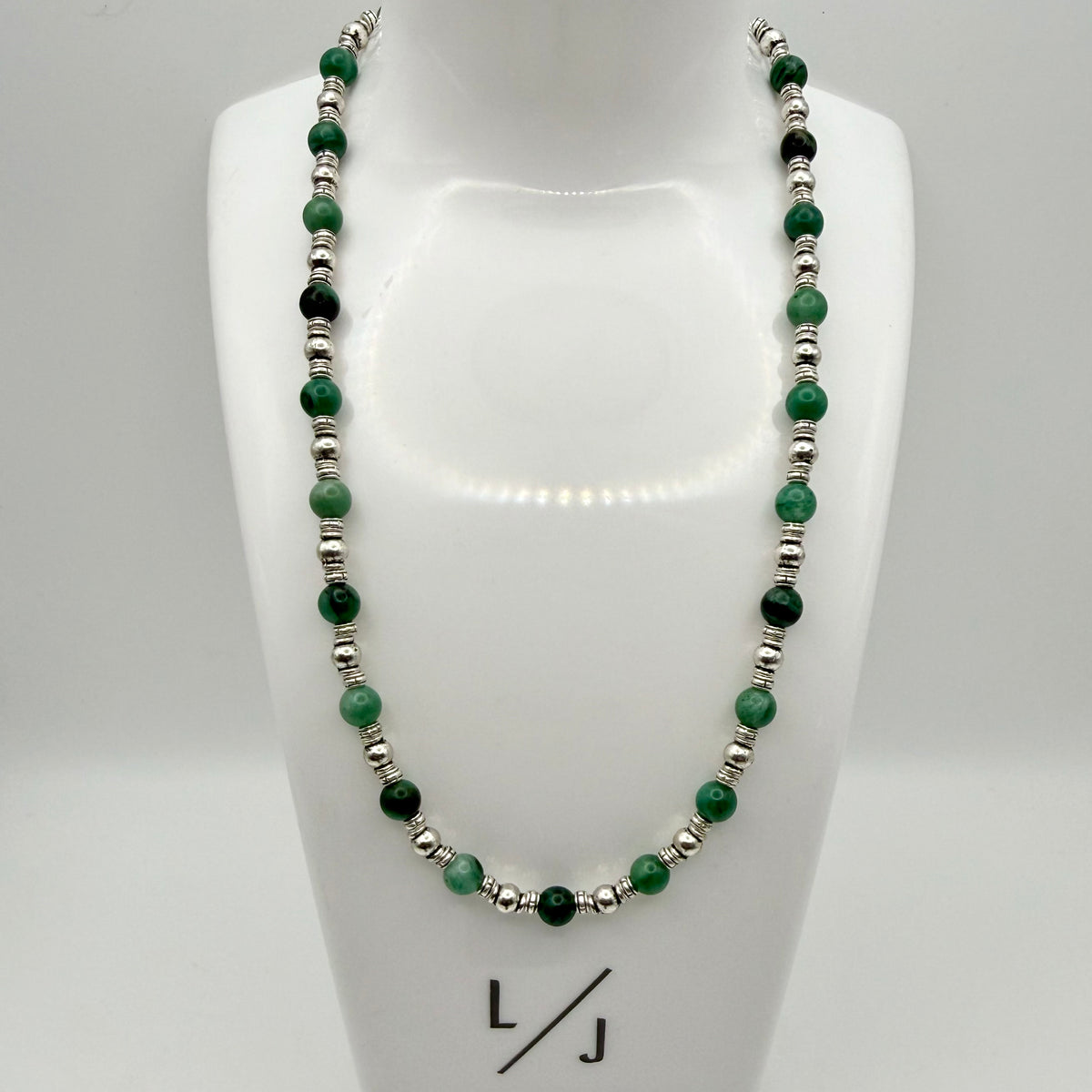 Necklace with green and silver beads on a mannequin bust, branded 'LJ'.