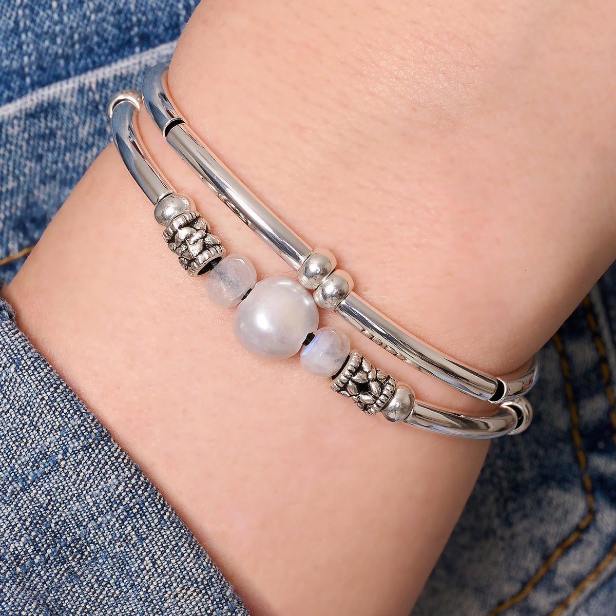 Silver bracelet with beads on a wrist against a denim background