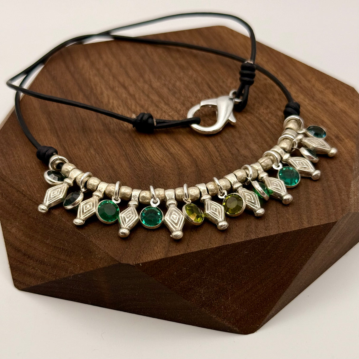 Bracelet with silver charms and green beads on a wooden block