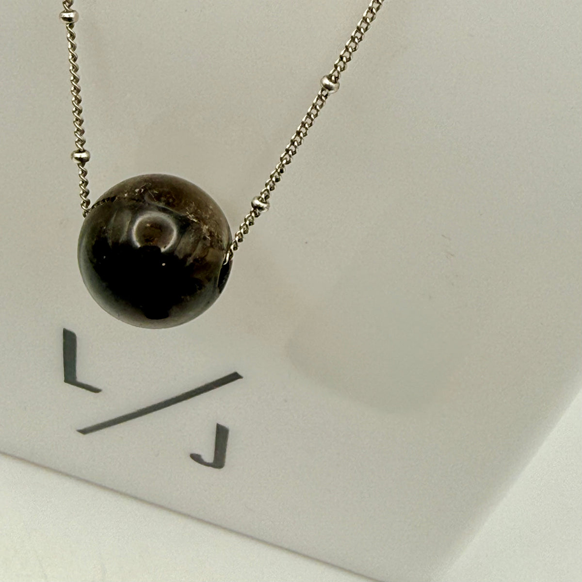 Necklace with a black bead pendant on a white card with 'LJ' initials.