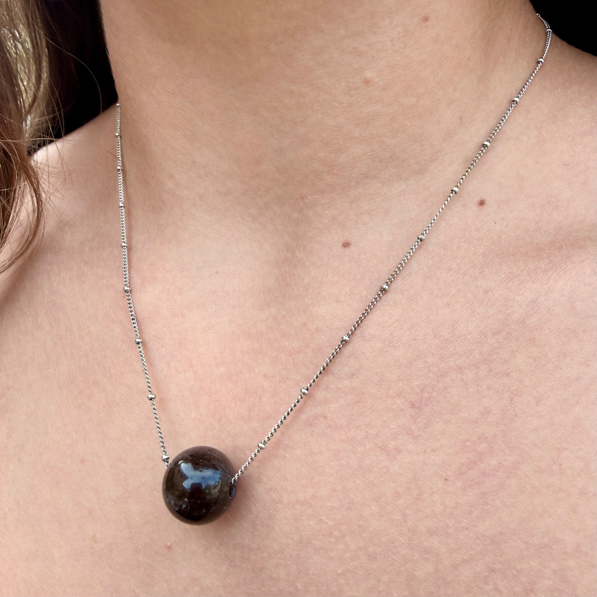 Necklace with a dark bead on a person's neck