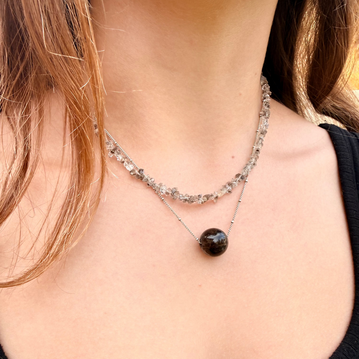 Necklace with a dark bead worn by a person with light skin and brown hair.