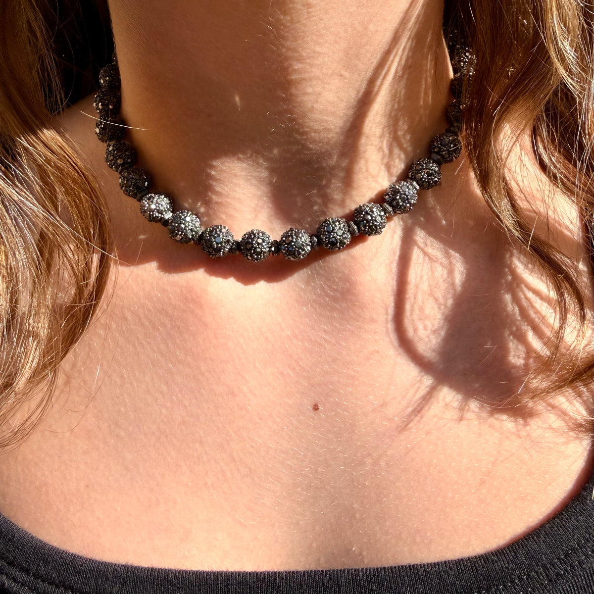 Necklace with dark beads worn by a person with blonde hair.