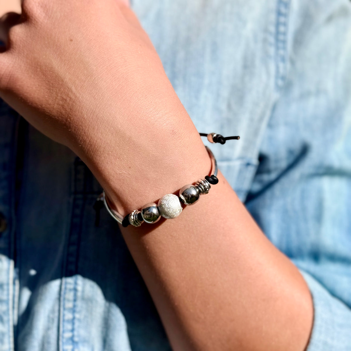 Close-up of a wrist wearing a bracelet with beads, against a blurred blue denim background.