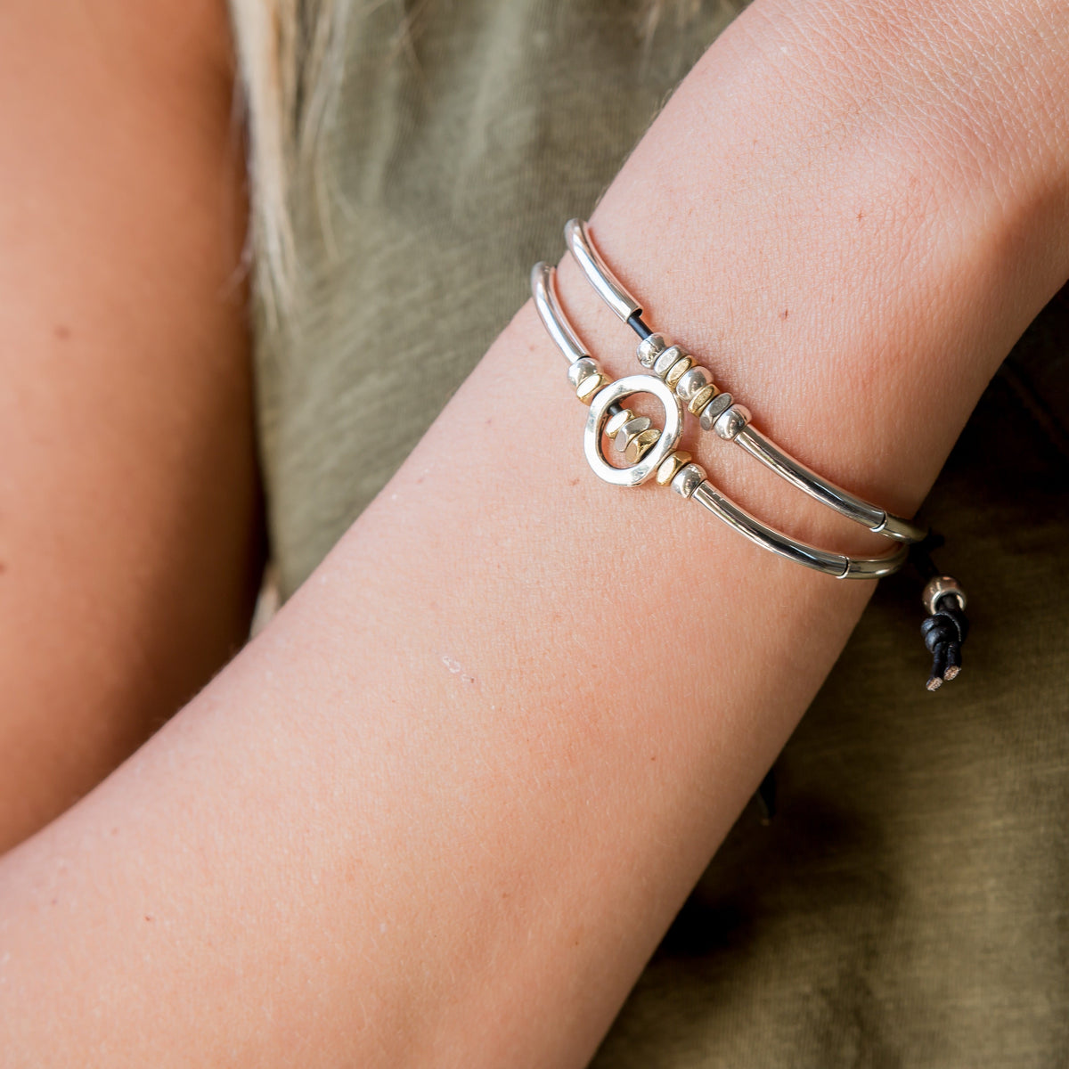 Close-up of a wrist wearing multiple silver bracelets on a neutral background