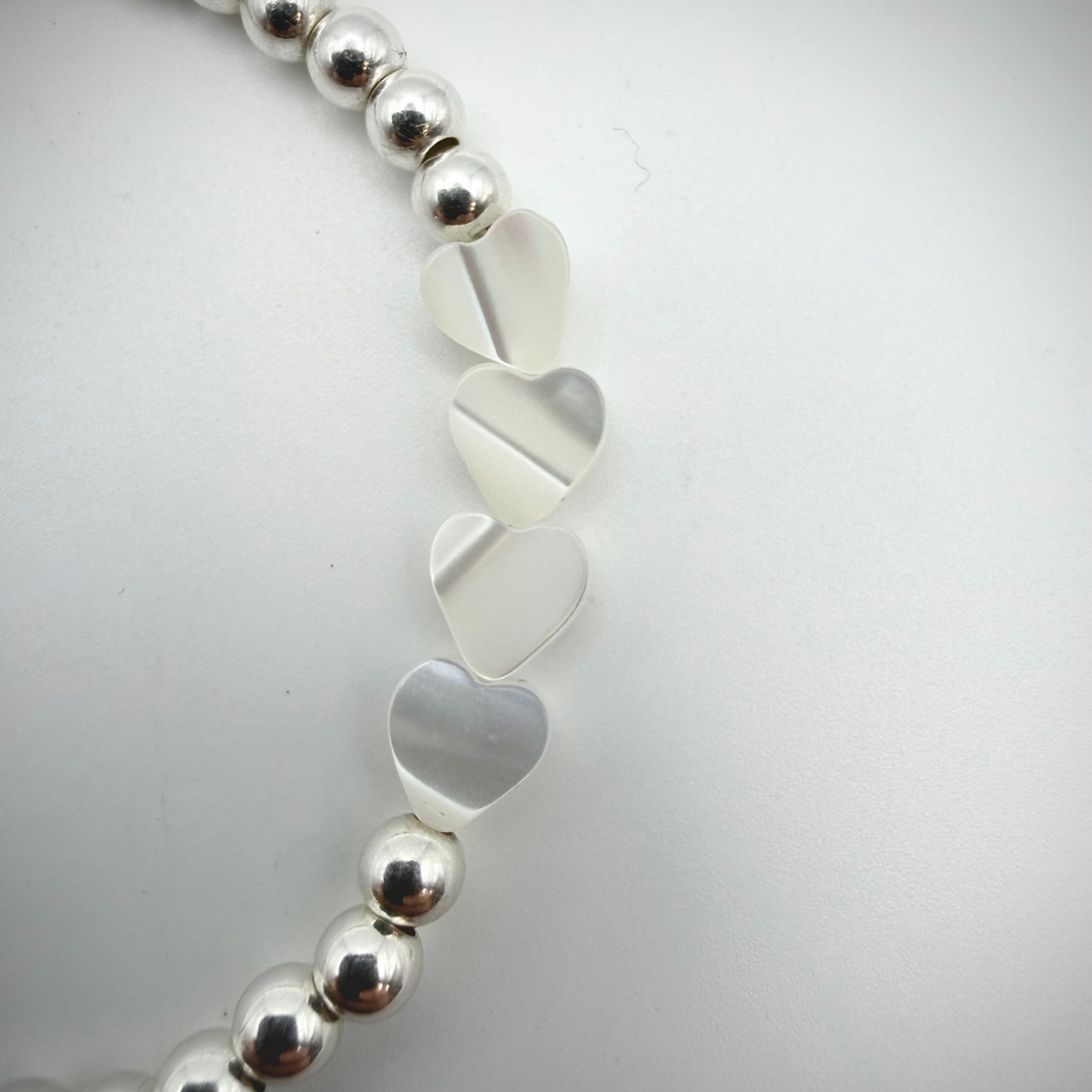 Silver beaded bracelet with heart-shaped charms on a light gray background