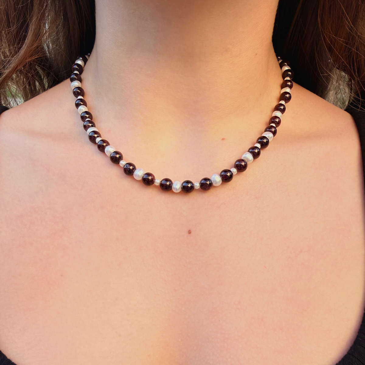 Necklace with brown and white beads on a person wearing a black top.