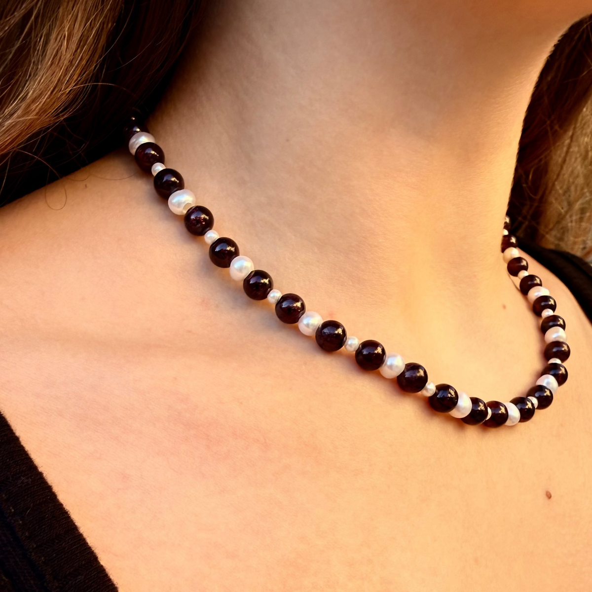 Necklace with black, white, and brown beads on a person wearing a black top.
