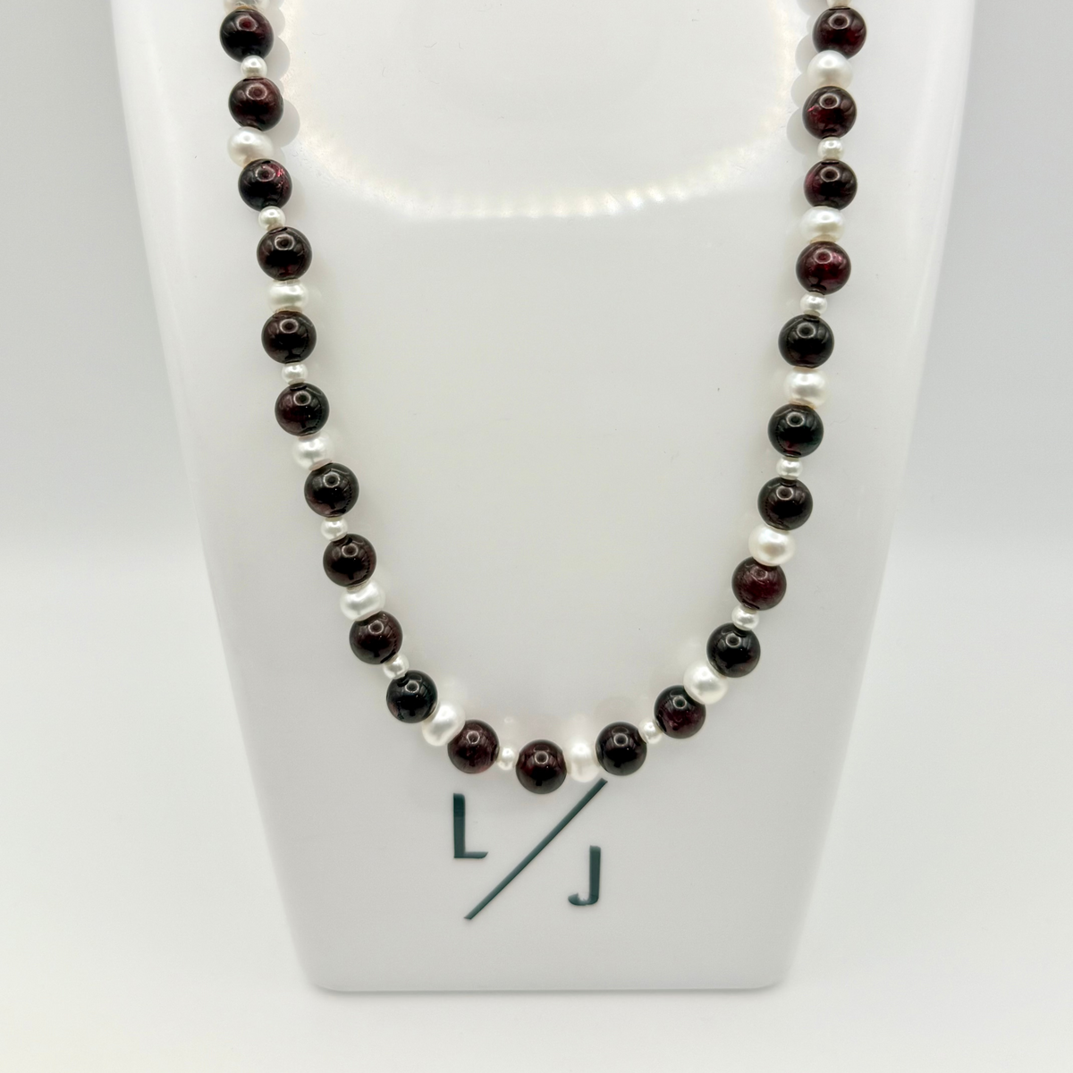 Necklace with alternating black and white beads on a white stand with a visible brand logo.