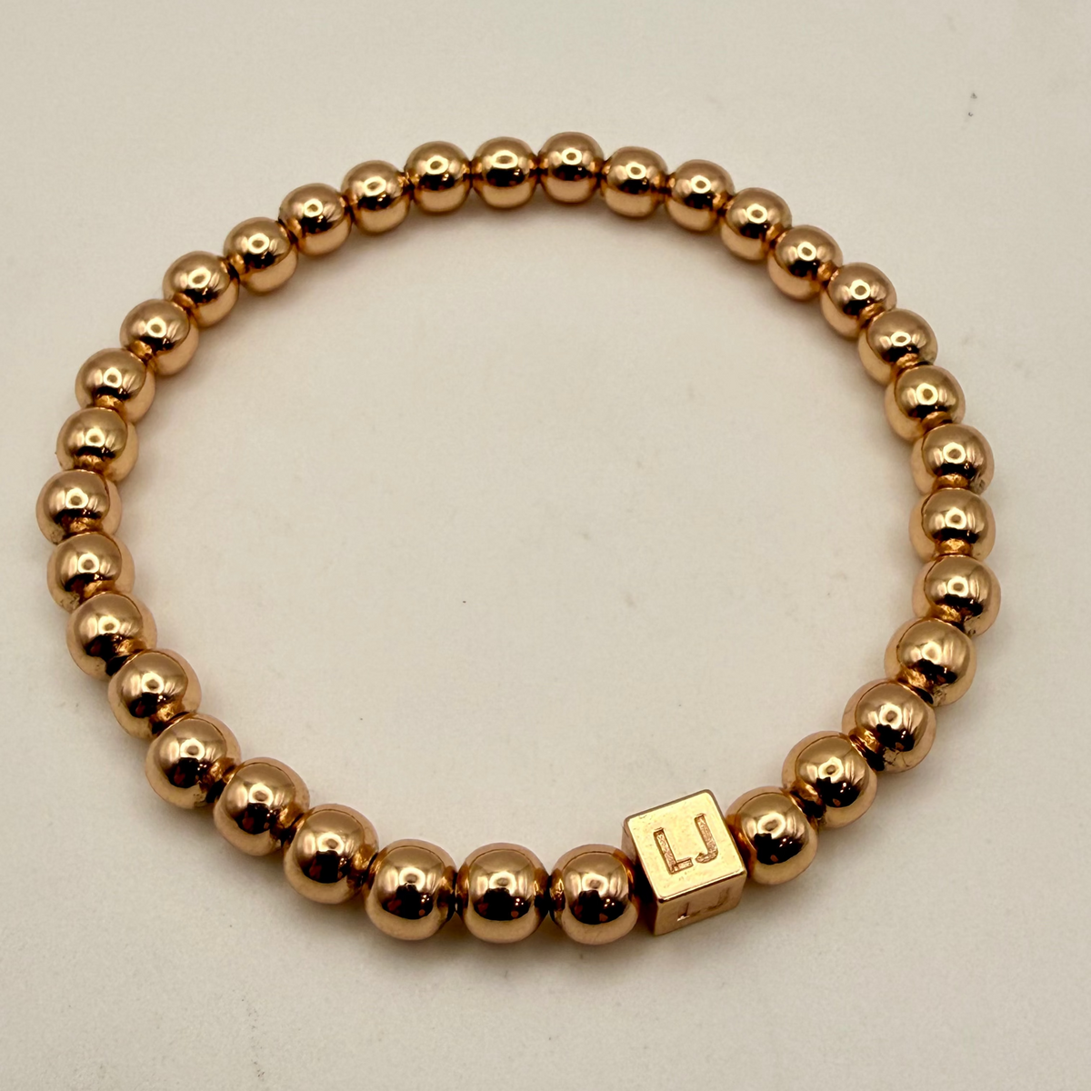 Gold beaded bracelet with a square charm on a light gray background